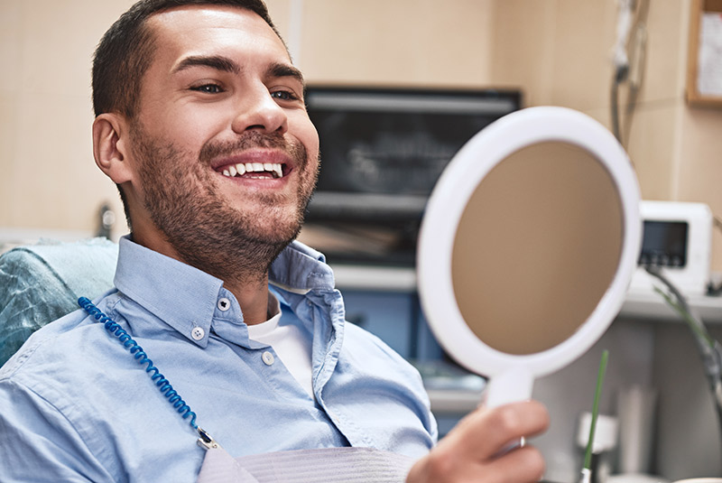 Nice guy smiling looking into mirror from dental chair